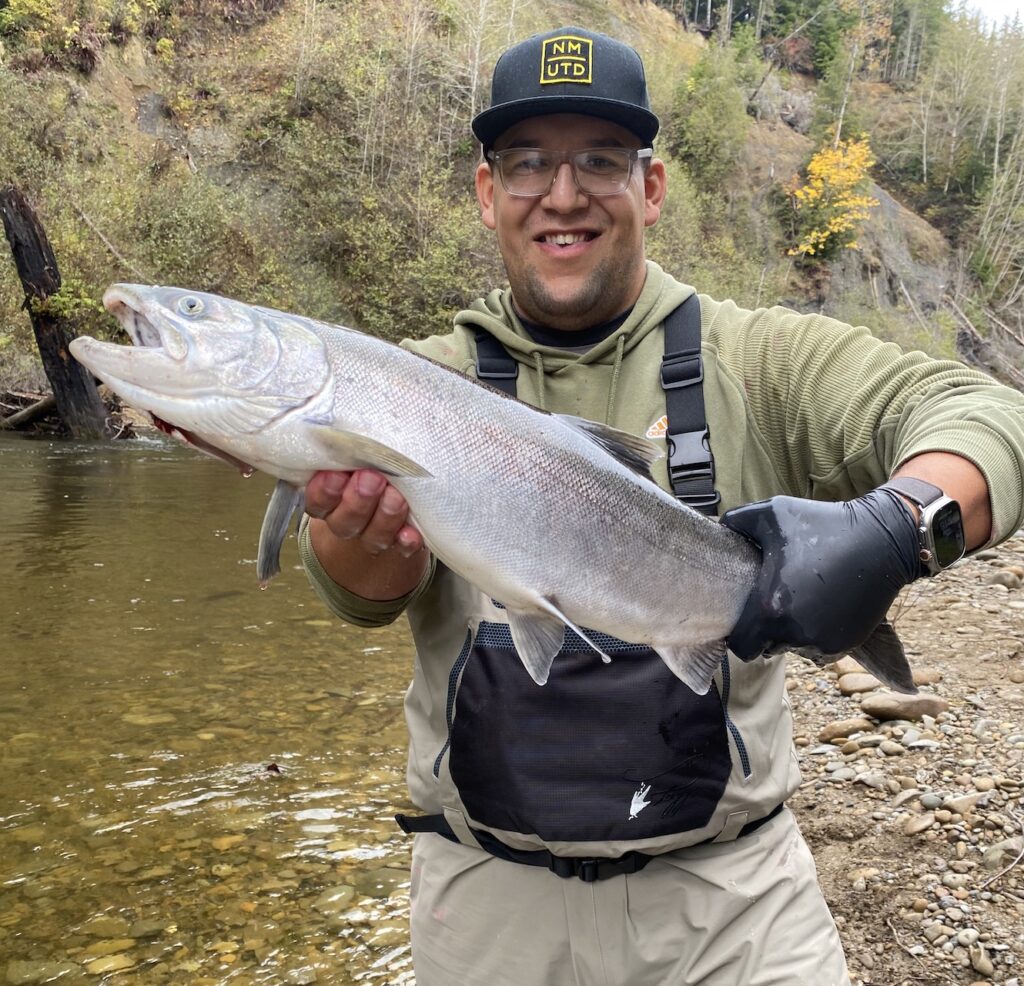 Daniel holding a chrome bright coho from a river